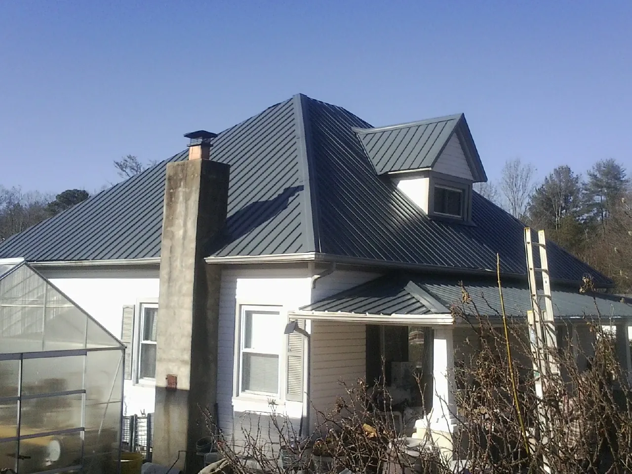 Dark blue standing seam metal roof on a white farmhouse with dormer — Slate & Tile Roof Repair by Roofing Brothers in Carbon Cliff