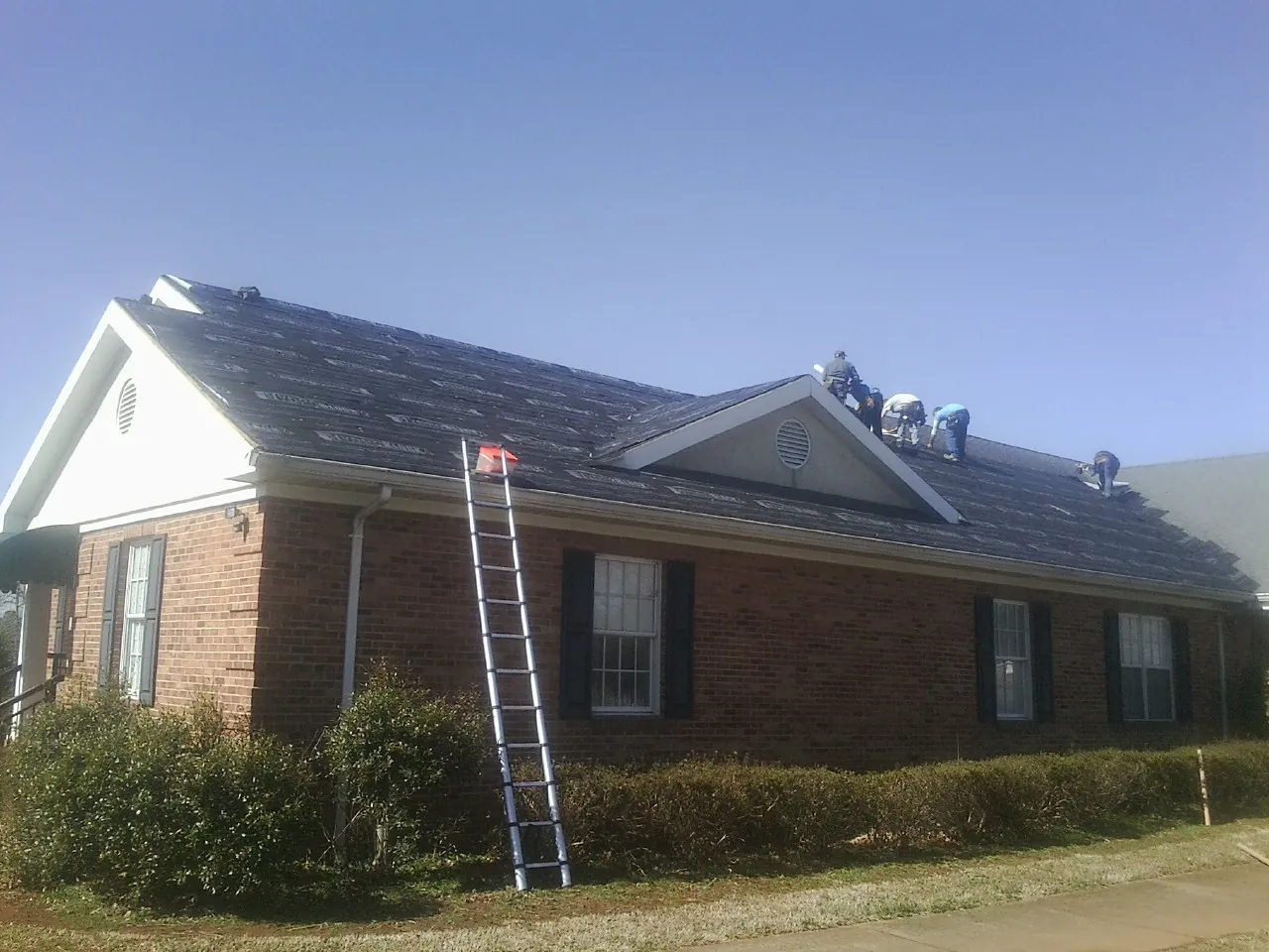 Crew tearing shingles off a brick ranch roof with a ladder set — Metal Roof Repair work by our crew in Carbon Cliff