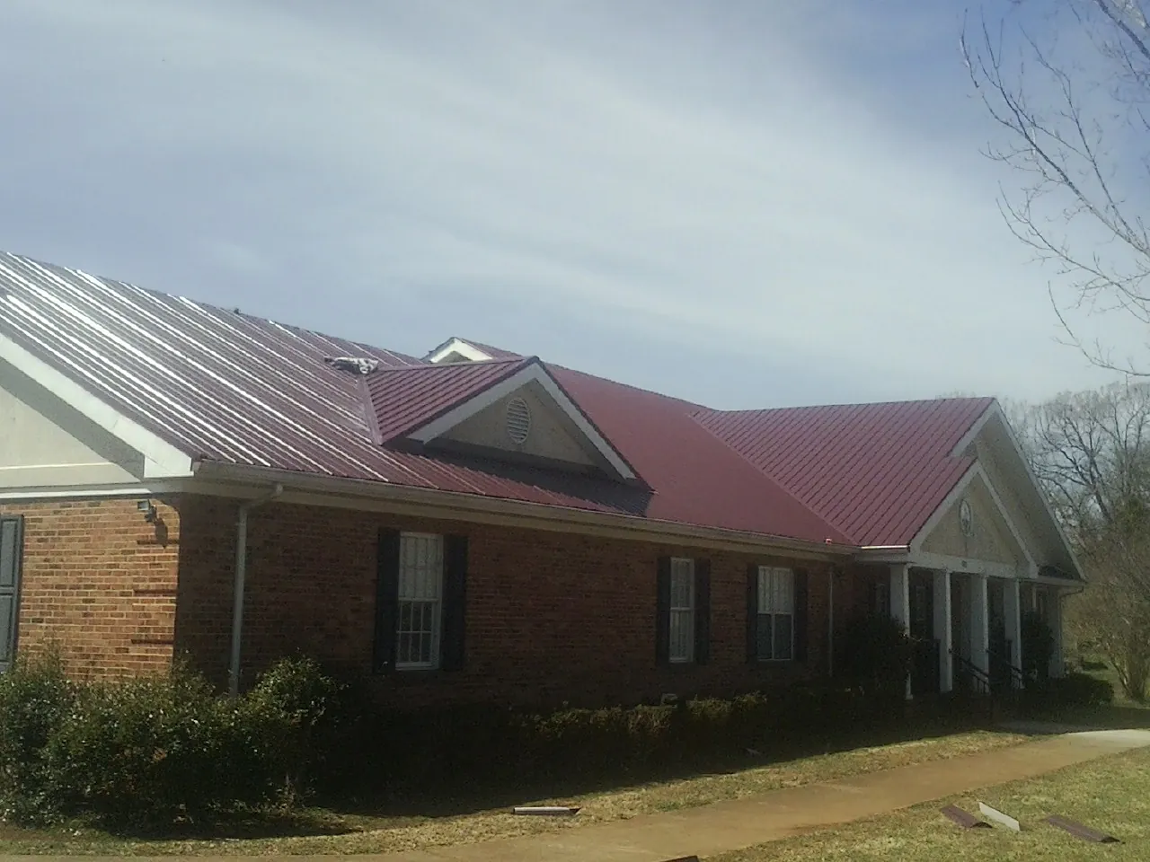 Red metal roof with gabled entries on a long brick building, from a Hail Damage Roof Repair job in Carbon Cliff
