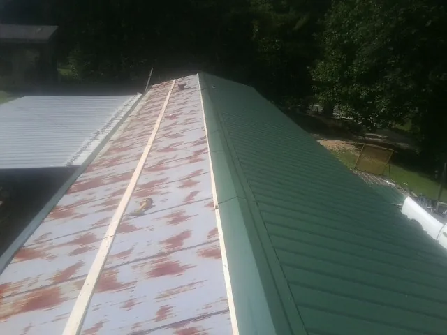Old rusted panels beside newly installed green metal roofing — Wind Damage Roof Repair by Roofing Brothers in Carbon Cliff