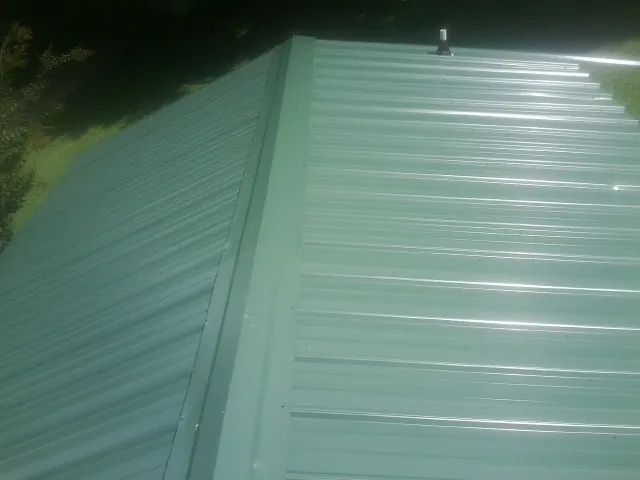 New green metal panels meeting at the ridge of a roof — Flat Roof Repair work by our crew in Carbon Cliff