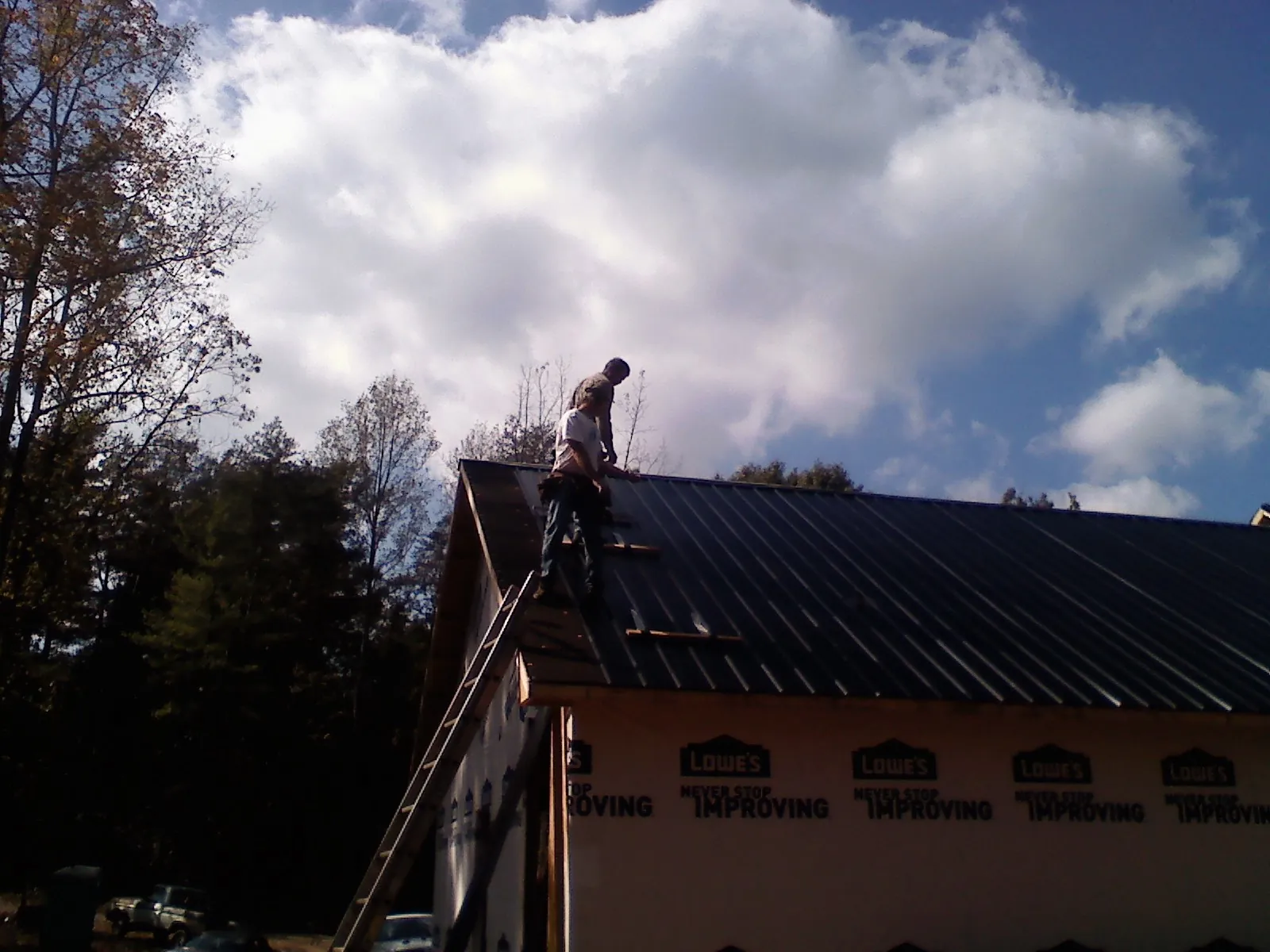 Roofer fastening dark metal panels high against a cloudy sky, from a Roof Inspection job in Carbon Cliff