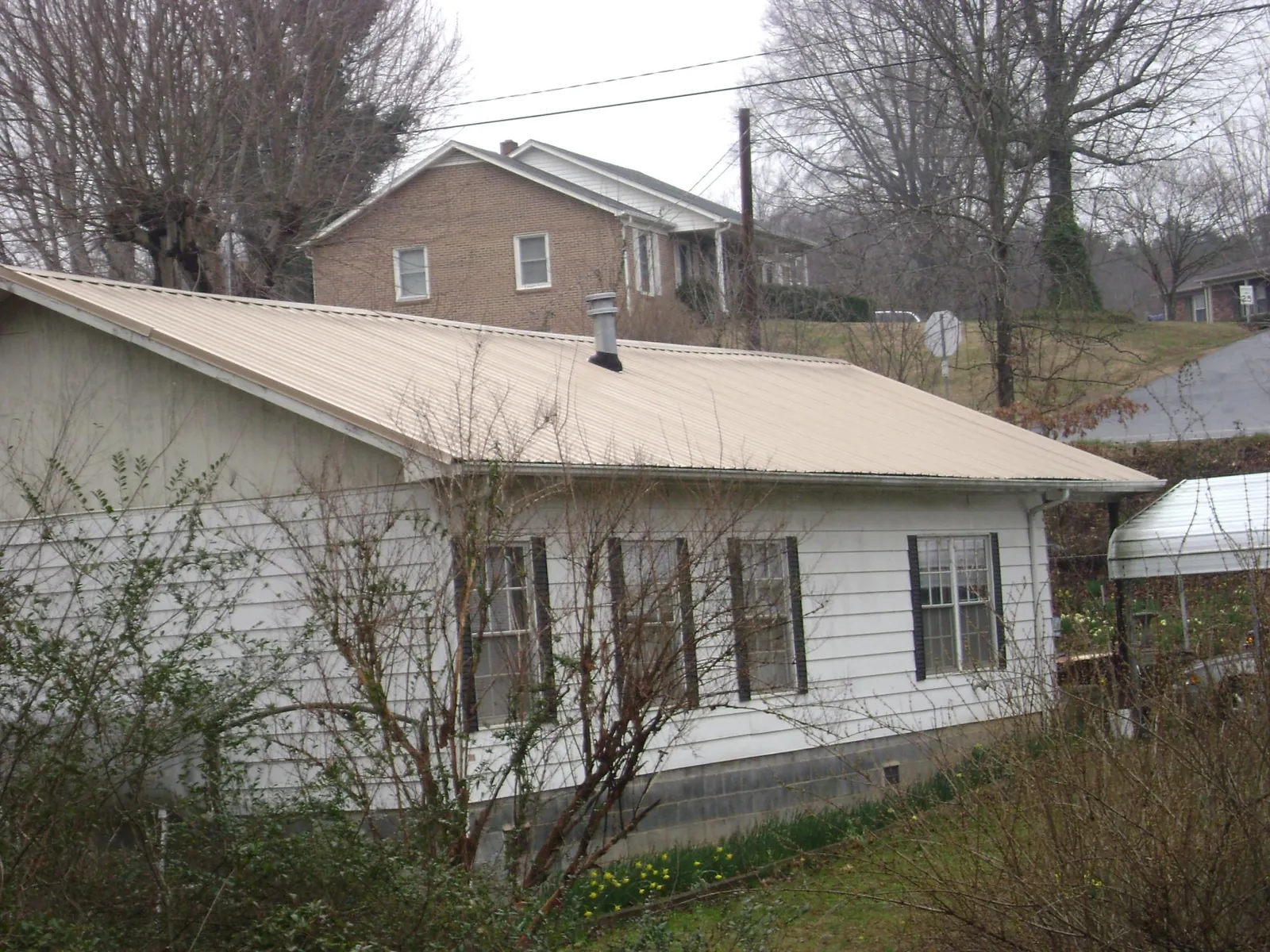 Tan metal roof on a white sided house set into a hillside — Commercial Roofing by Roofing Brothers in Carbon Cliff