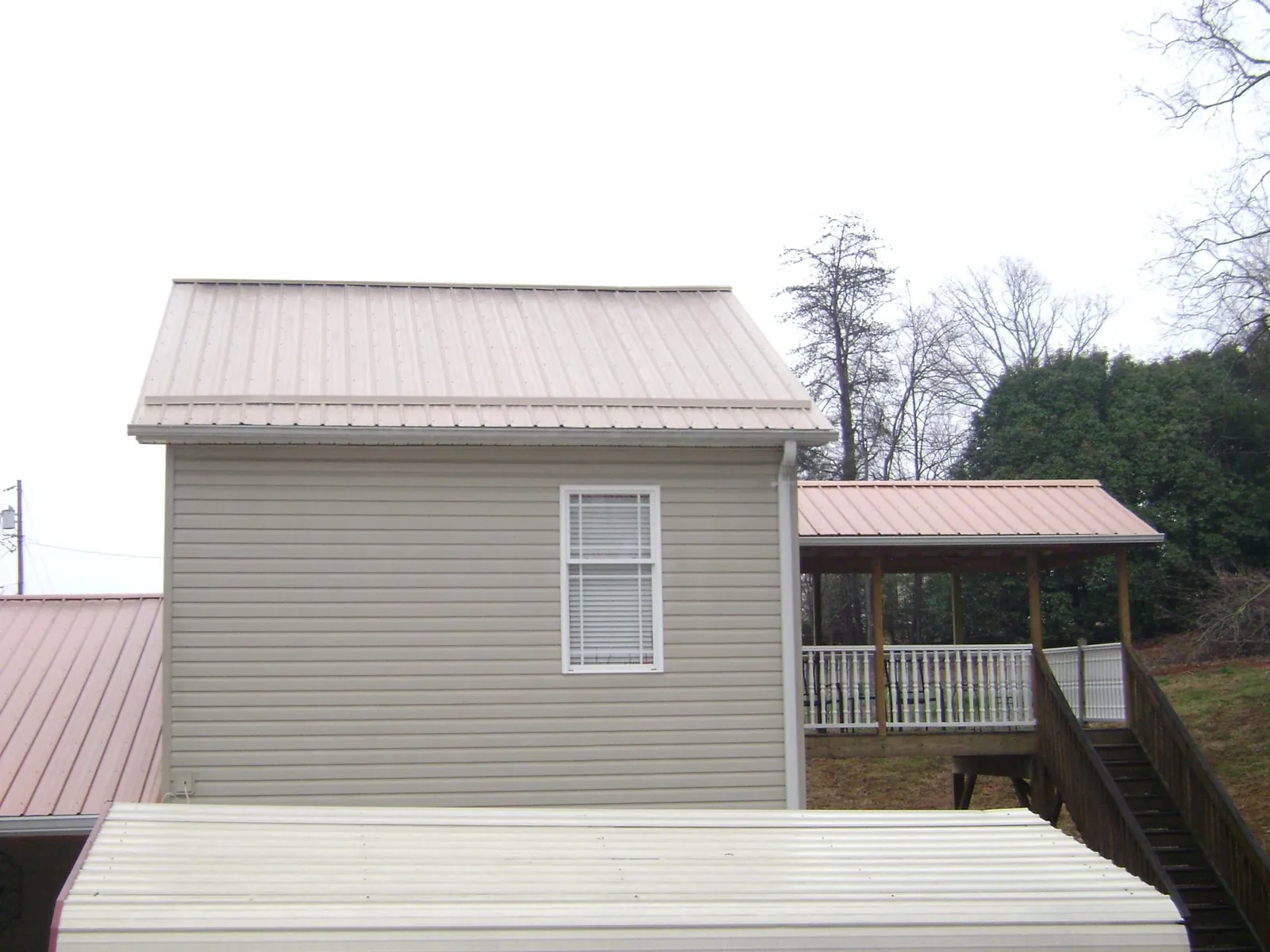 Tan metal roofs on a two story addition and attached porch, from a Roof Replacement job in Carbon Cliff