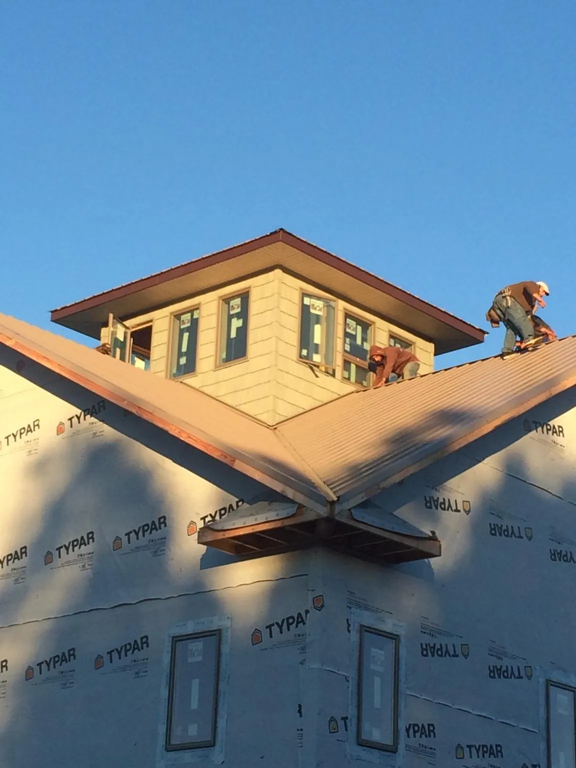 Roofers working around a rooftop cupola on a new metal roof at sunset — Roof Waterproofing in Carbon Cliff by Roofing Brothers